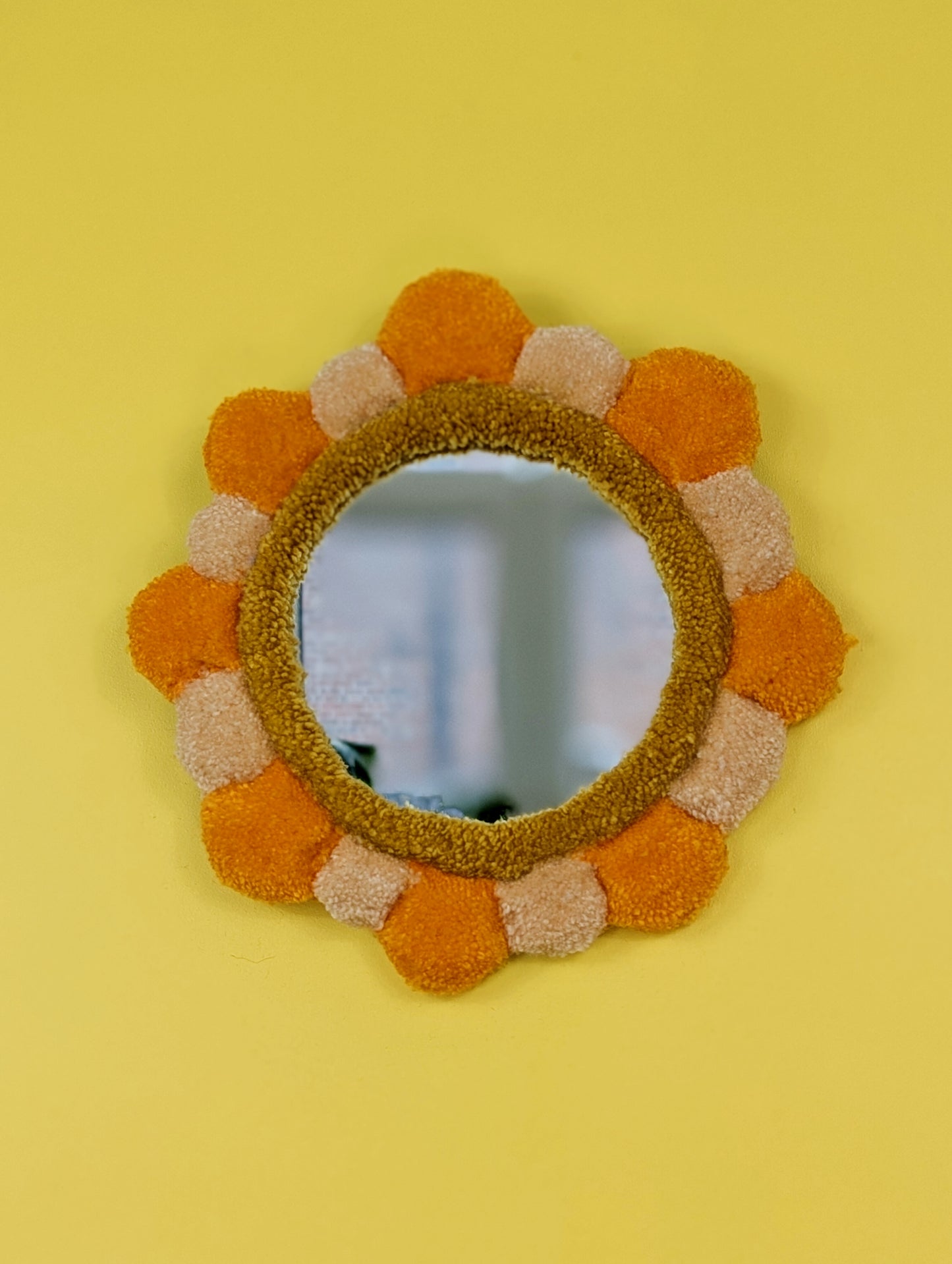 Handmade tufted petal mirror with alternating orange and beige textured yarn petals surrounding a round mirror