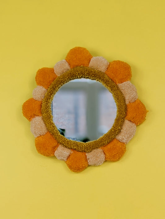 Handmade tufted petal mirror with alternating orange and beige textured yarn petals surrounding a round mirror