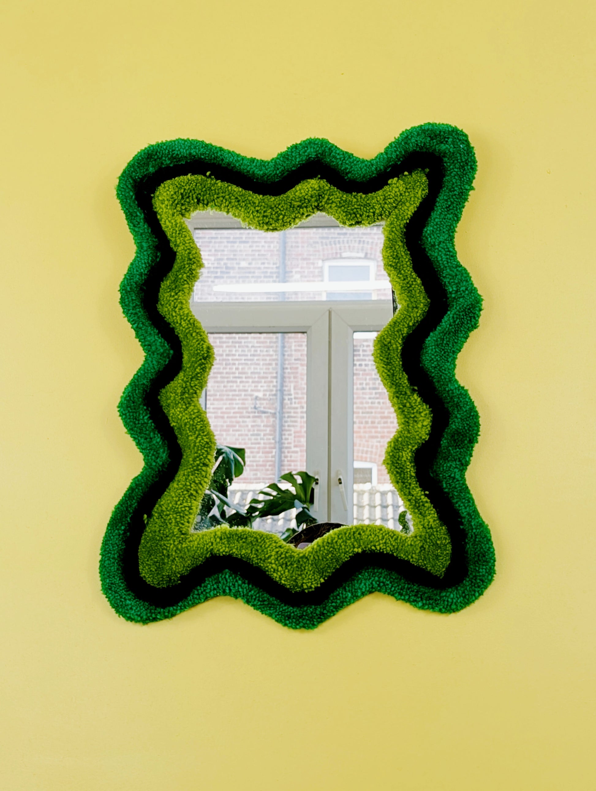 Handmade wavy tufted mirror with colourful textured frame in alternating shades of green, modern aesthetic wall décor for home interiors.