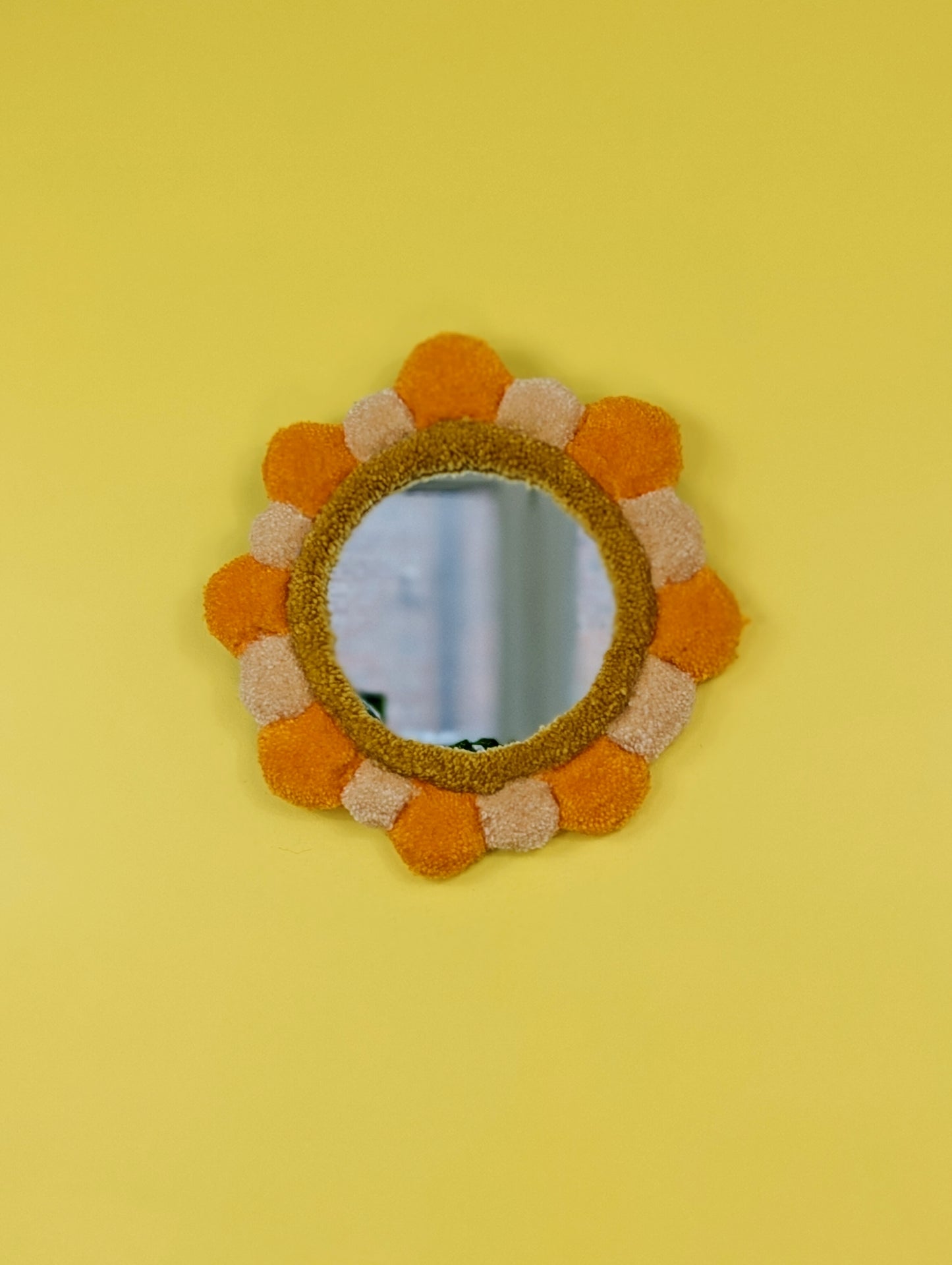 Handmade tufted petal mirror with alternating orange and beige textured yarn petals surrounding a round mirror