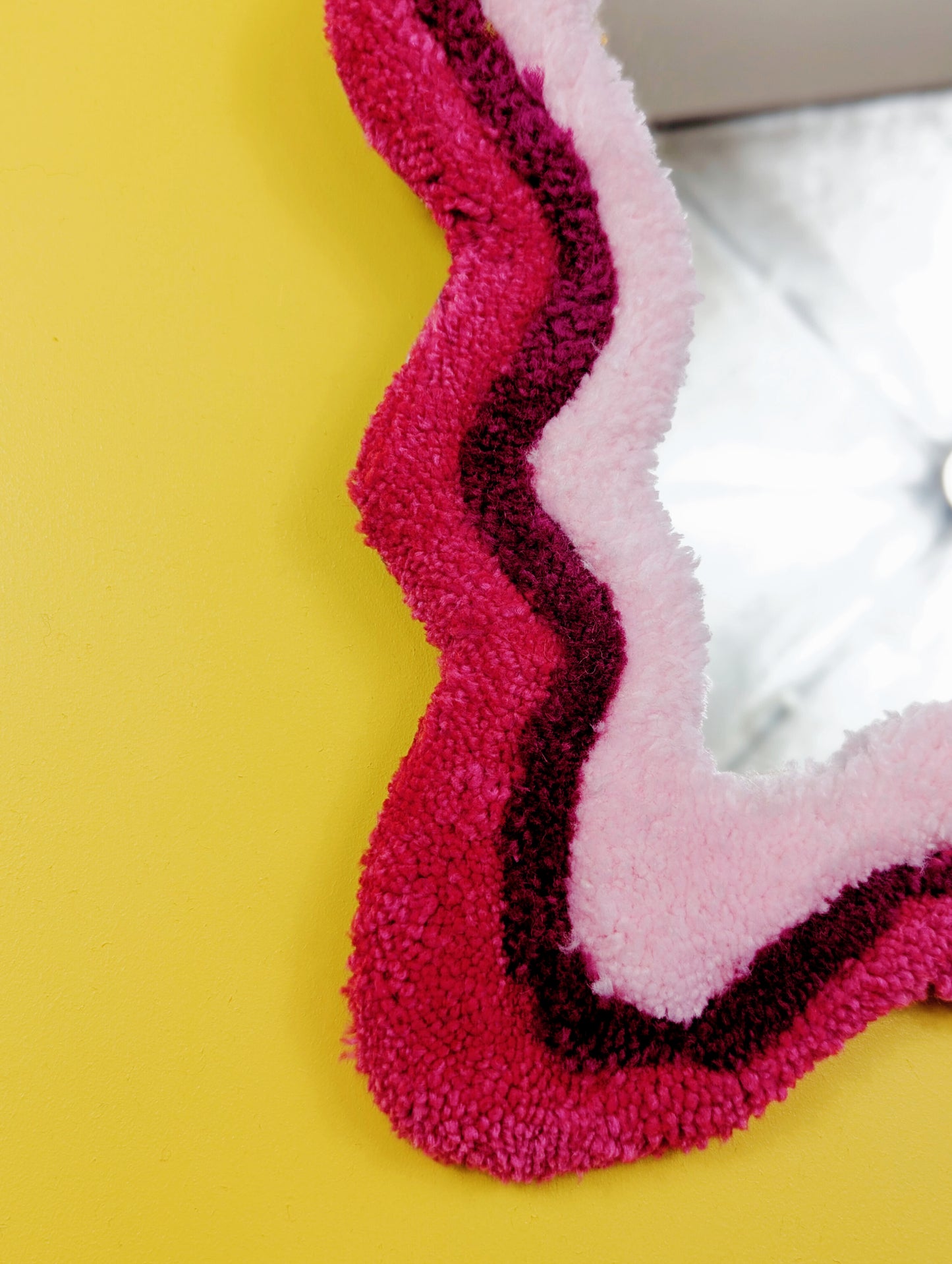 Handmade wavy tufted mirror with colourful textured frame in alternating shades of pink, modern aesthetic wall décor for home interiors.