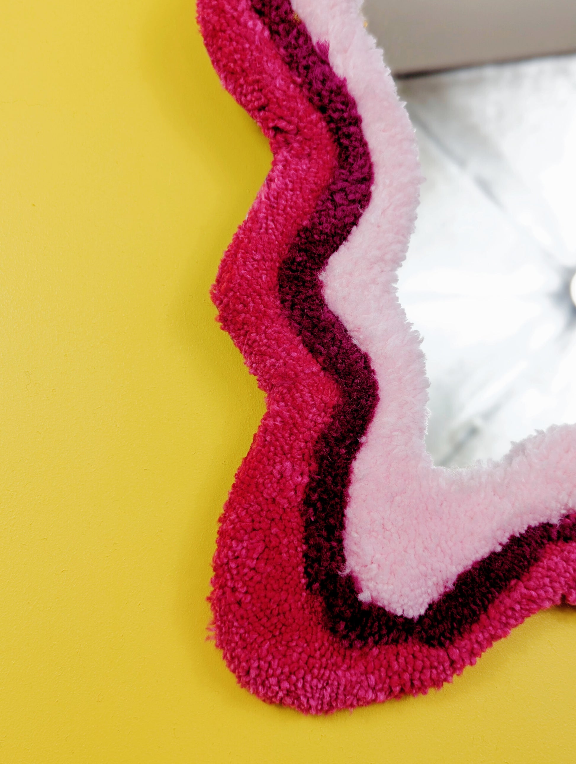 Handmade wavy tufted mirror with colourful textured frame in alternating shades of pink, modern aesthetic wall décor for home interiors.