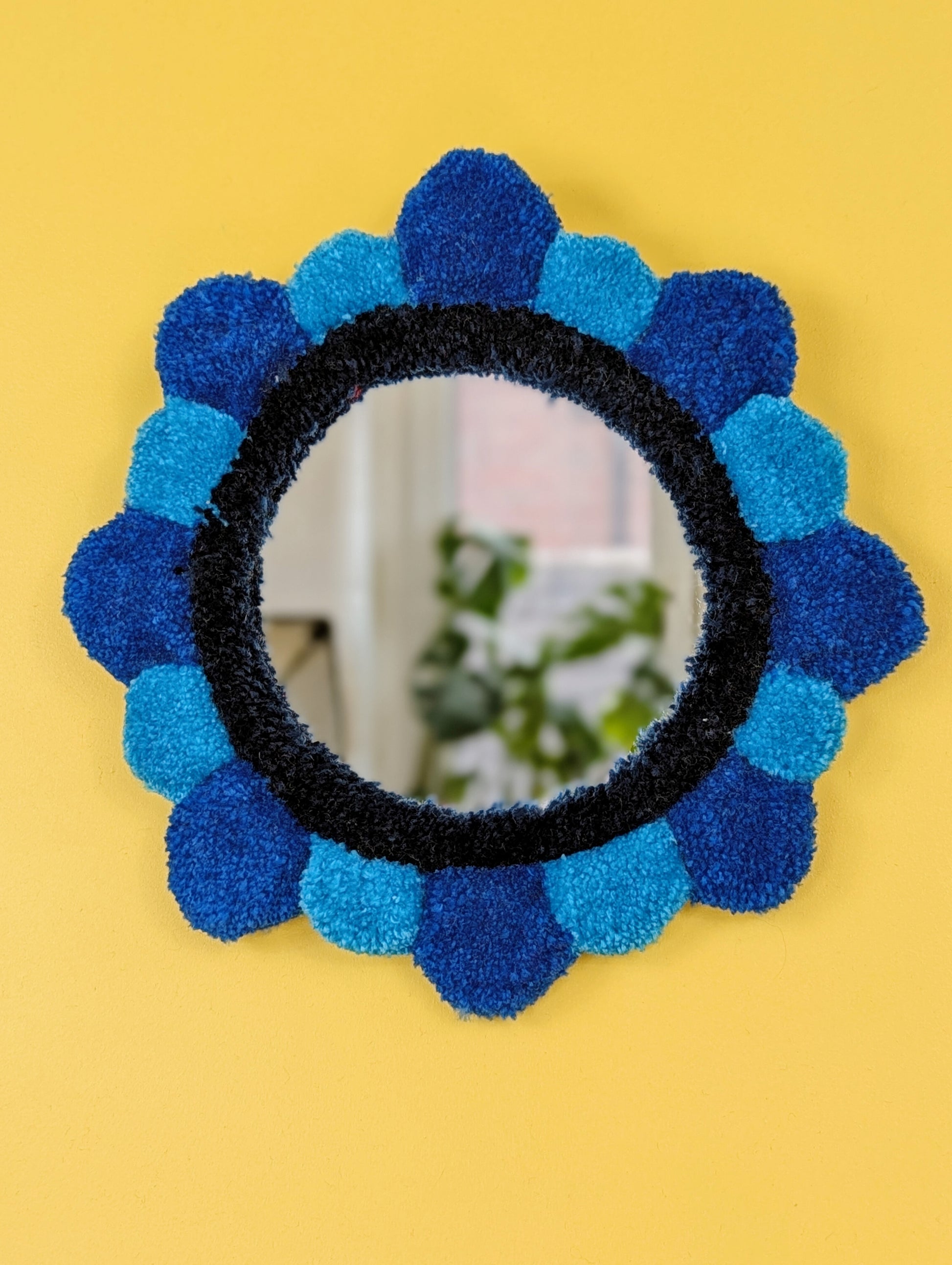 Handmade tufted petal mirror with blue textured yarn petals surrounding a round mirror