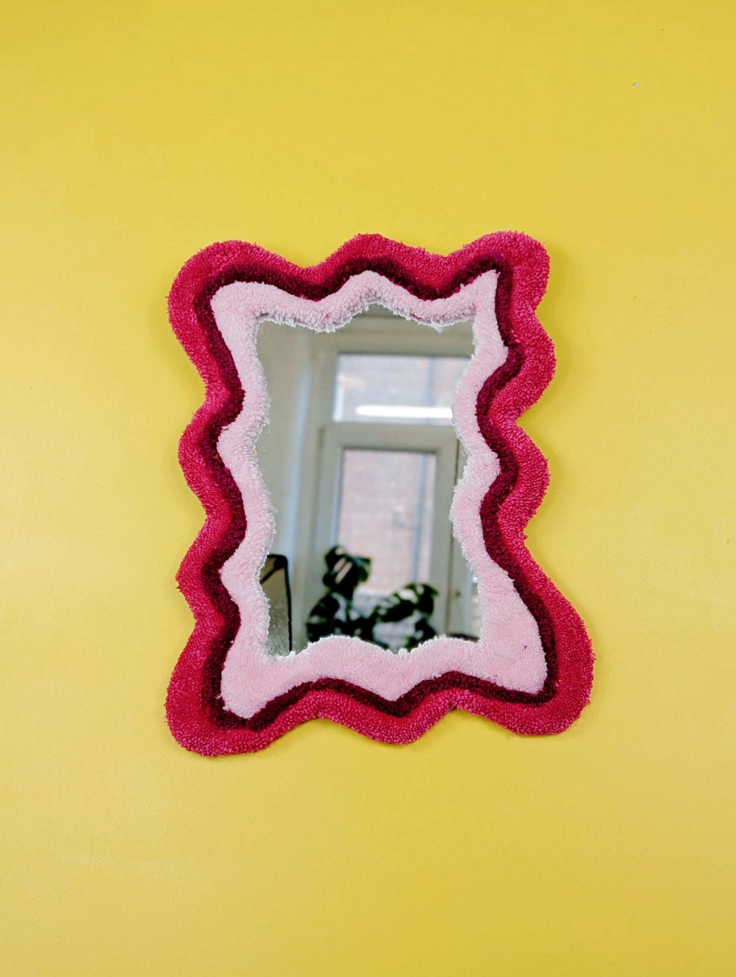 Handmade wavy tufted mirror with colourful textured frame in alternating shades of pink, modern aesthetic wall décor for home interiors.