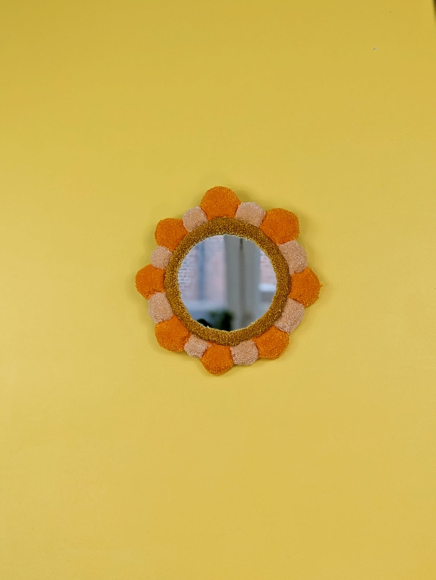 Handmade tufted petal mirror with alternating orange and beige textured yarn petals surrounding a round mirror
