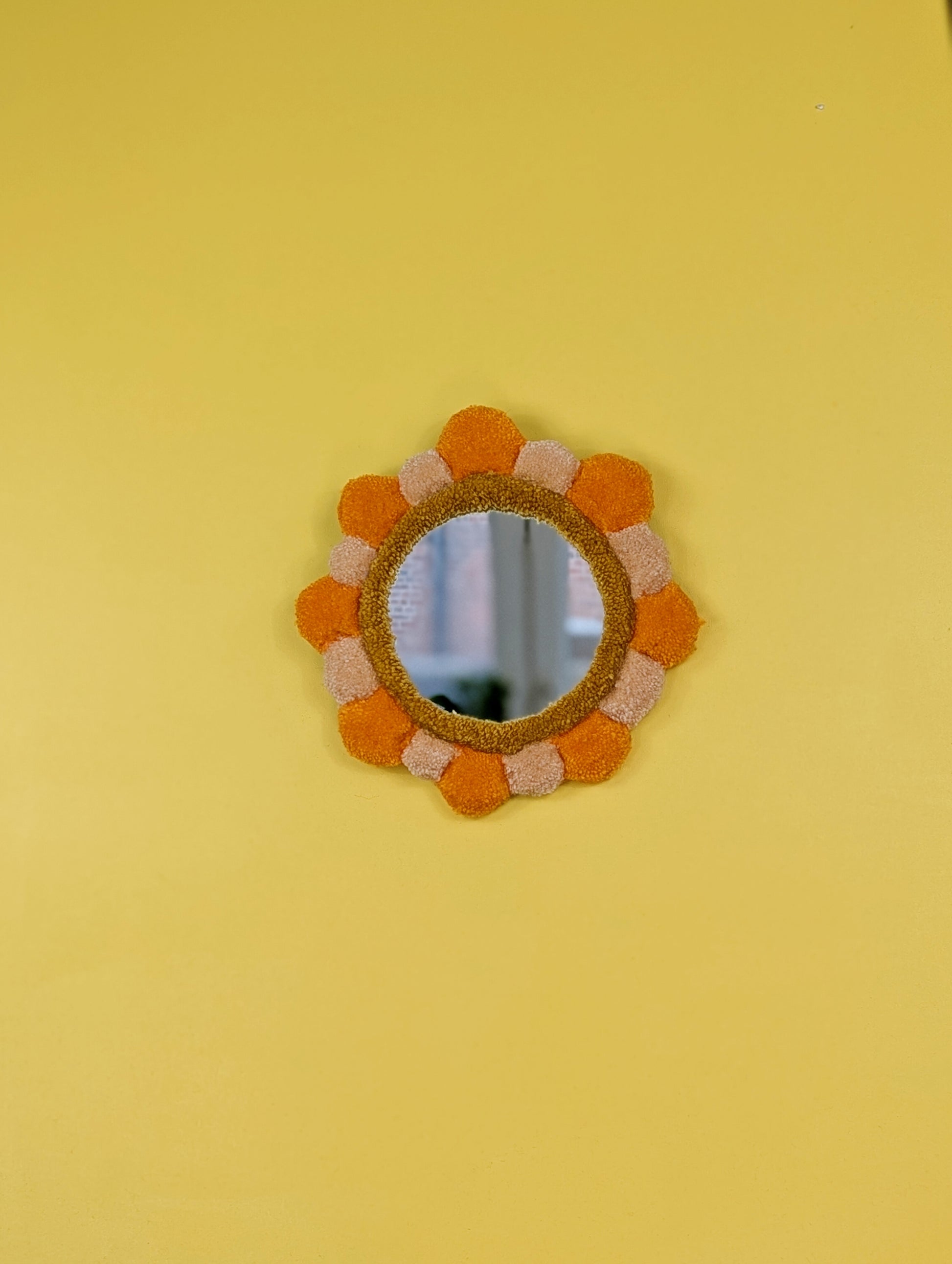 Handmade tufted petal mirror with alternating orange and beige textured yarn petals surrounding a round mirror