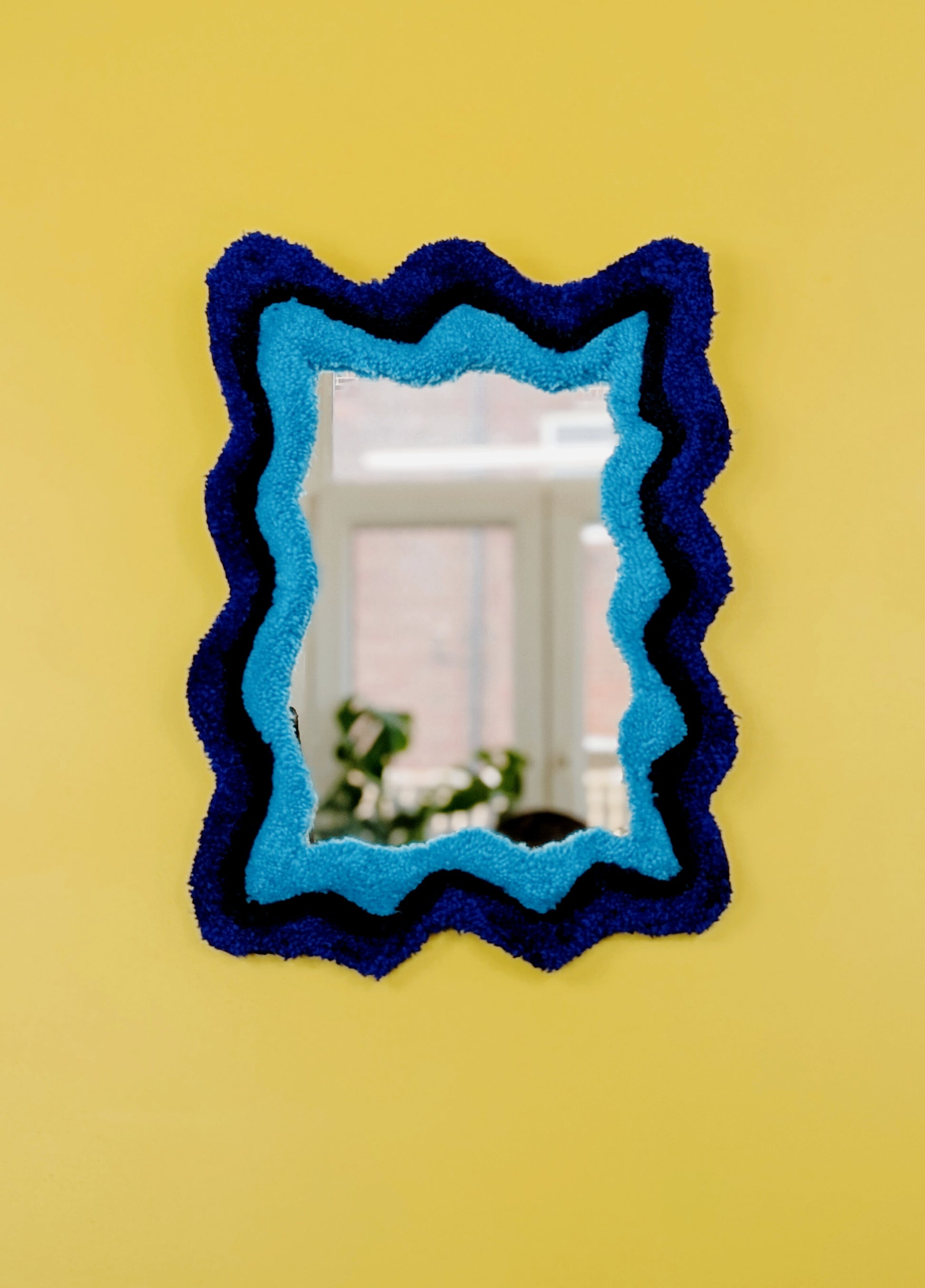 Handmade wavy tufted mirror with colourful textured frame in alternating shades of blue, modern aesthetic wall décor for home interiors.