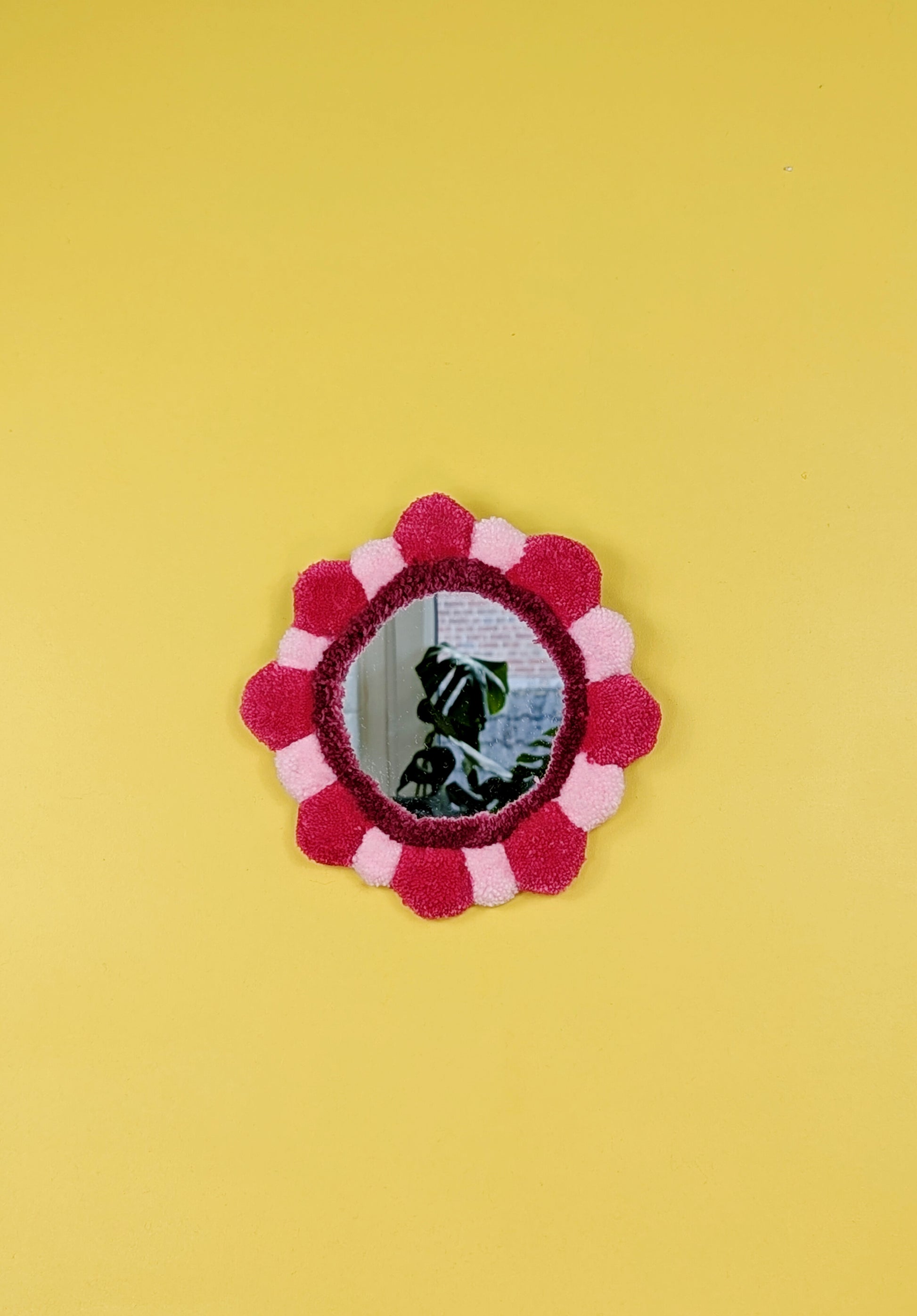 Handmade tufted petal mirror with pink textured yarn petals surrounding a round mirror