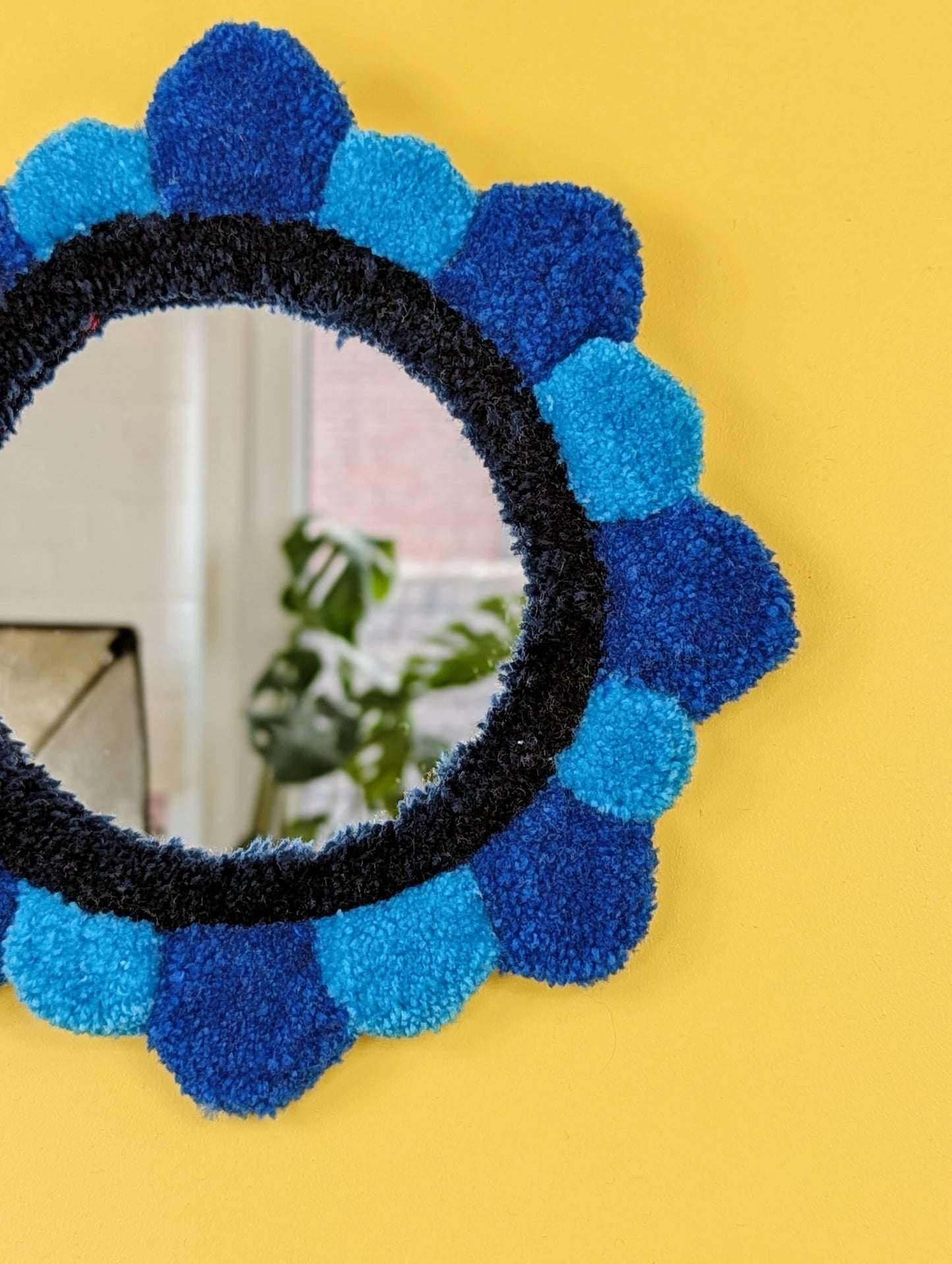 Handmade tufted petal mirror with blue textured yarn petals surrounding a round mirror