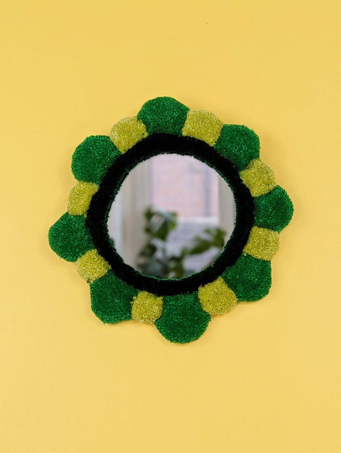 Handmade tufted petal mirror with green textured yarn petals surrounding a round mirror