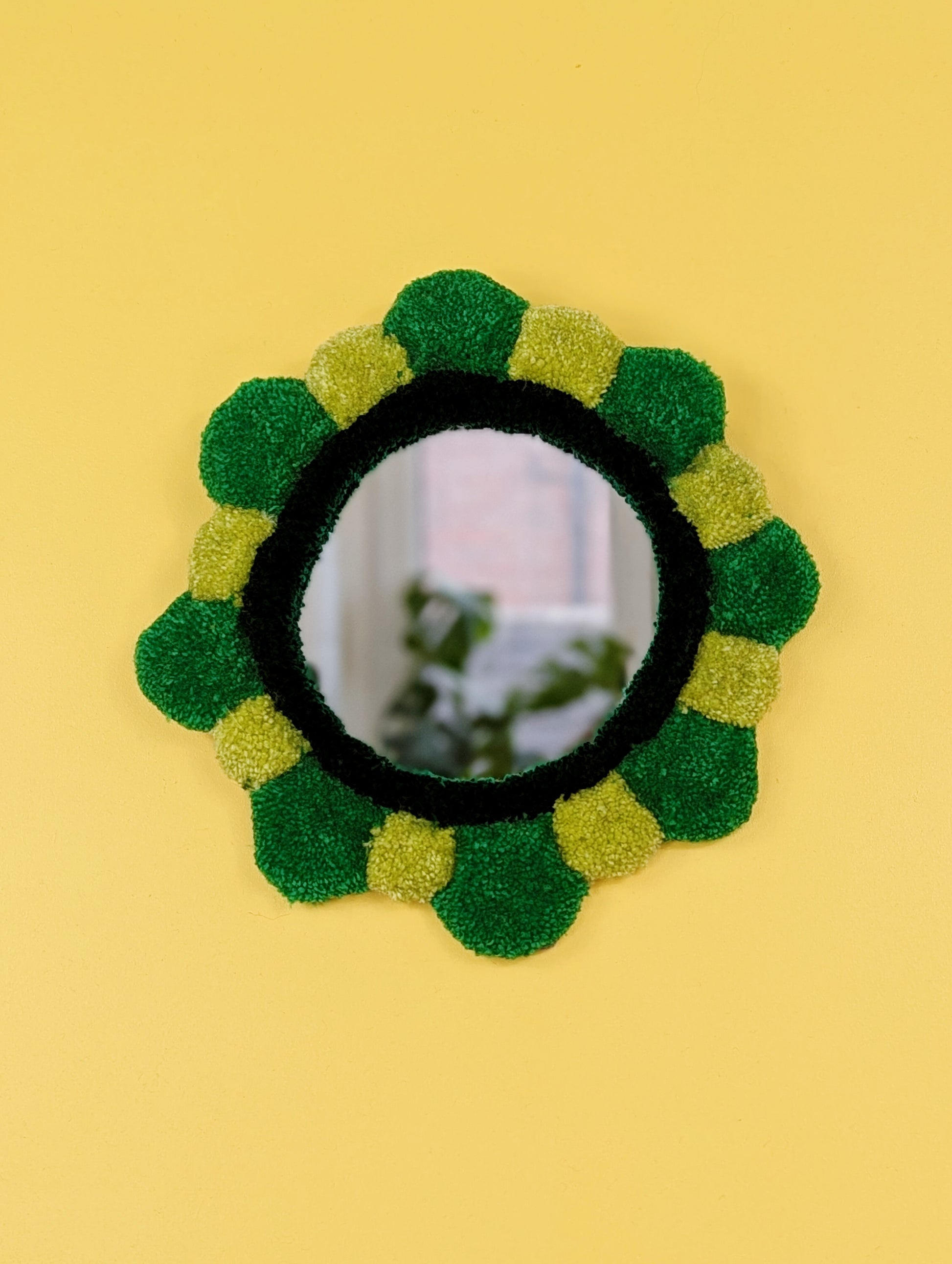 Handmade tufted petal mirror with green textured yarn petals surrounding a round mirror
