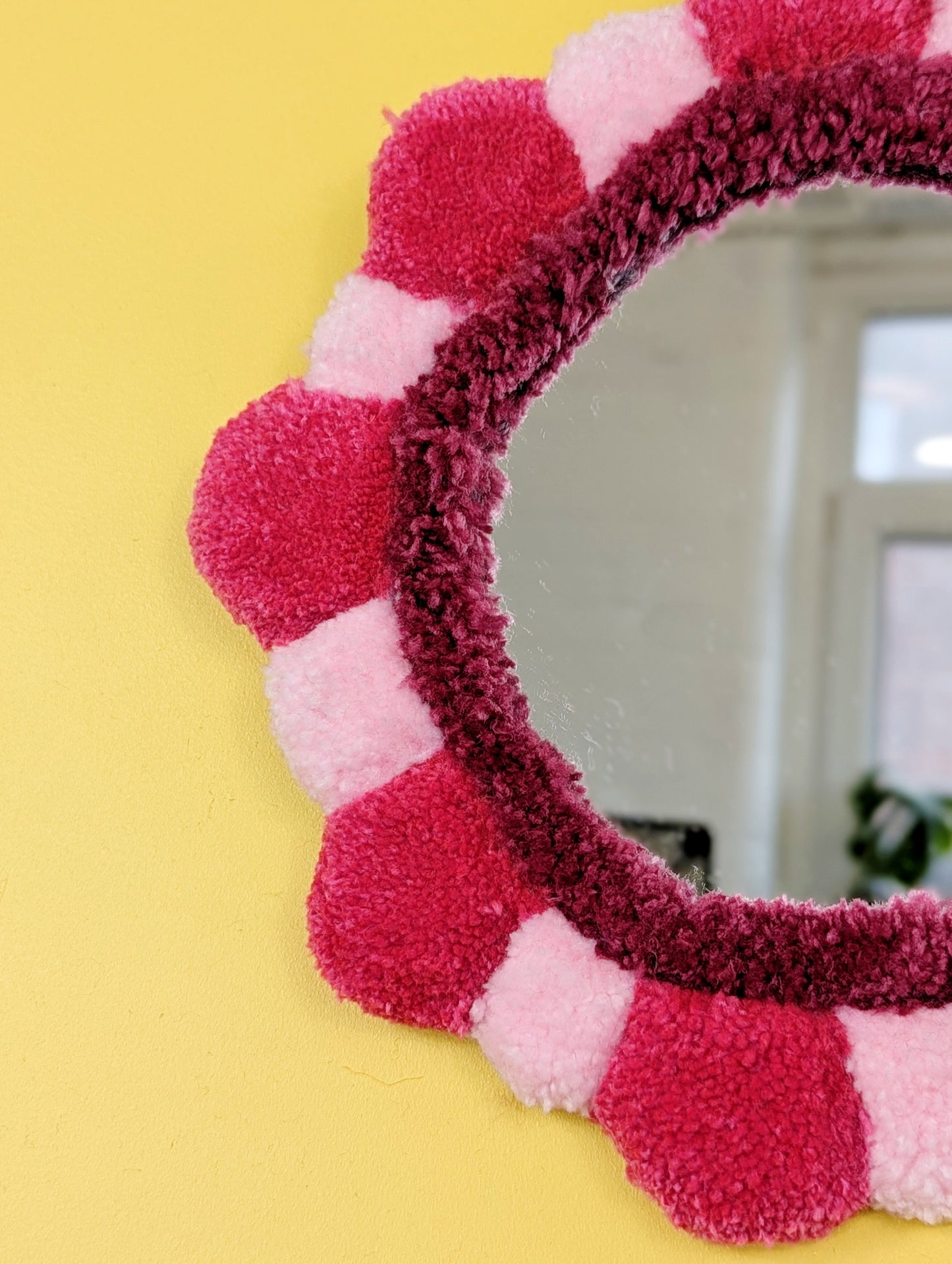 Handmade tufted petal mirror with pink textured yarn petals surrounding a round mirror