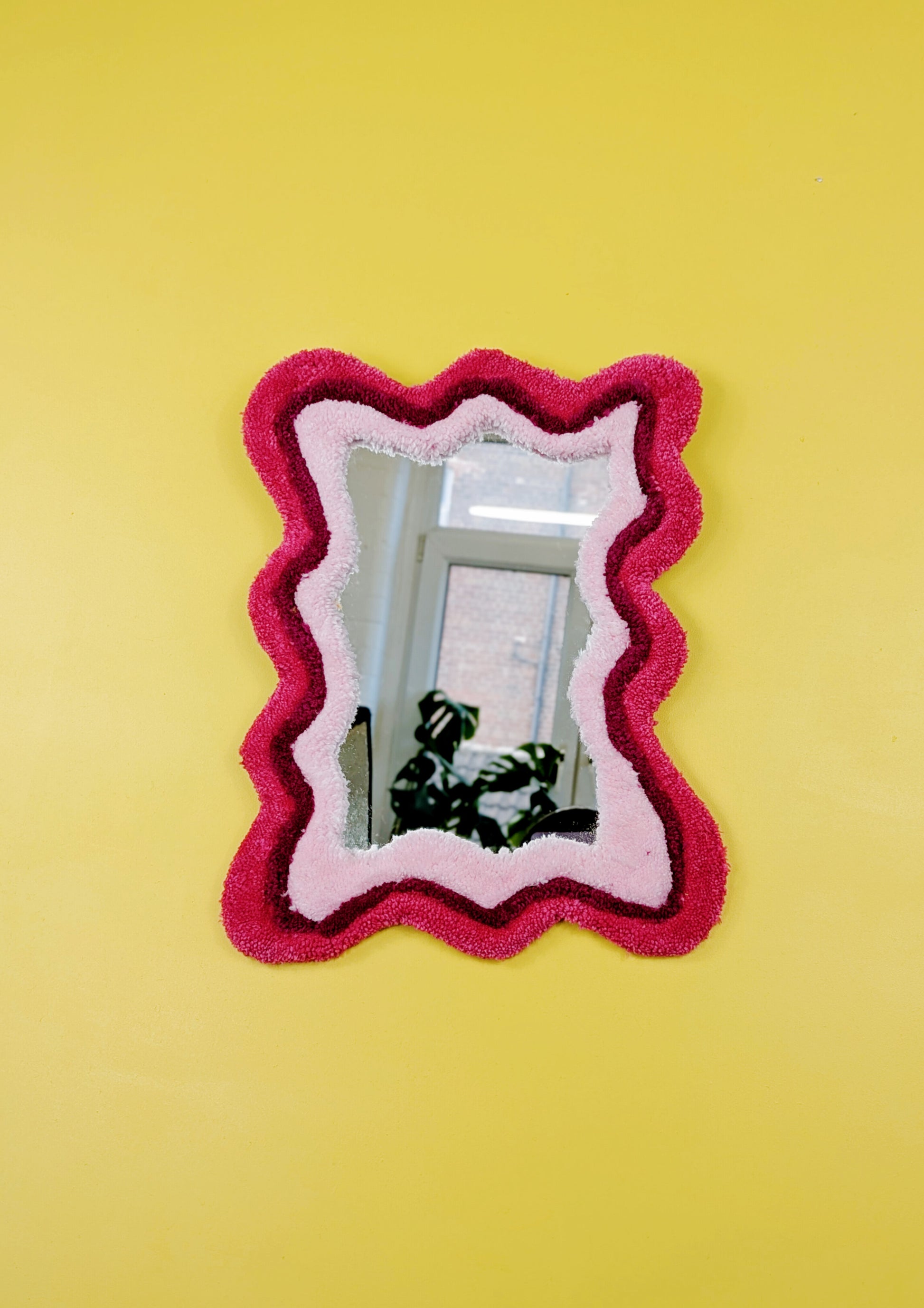 Handmade wavy tufted mirror with colourful textured frame in alternating shades of pink, modern aesthetic wall décor for home interiors.