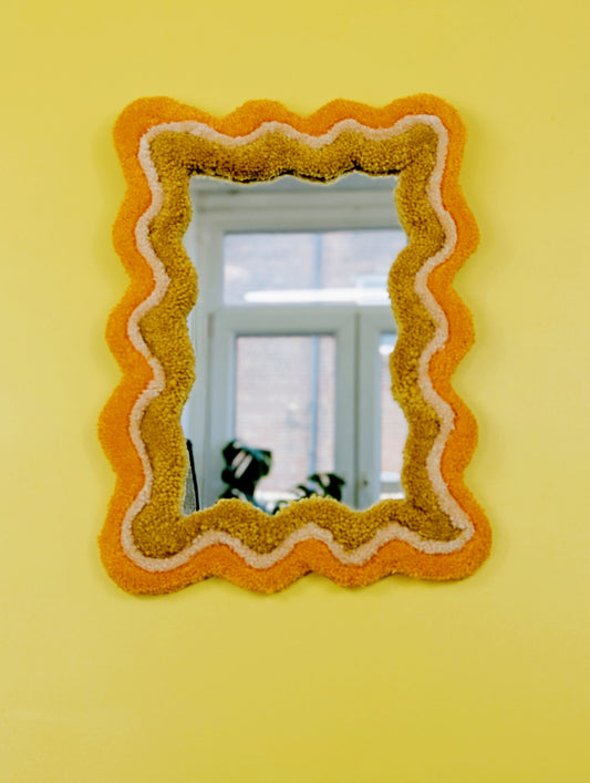 Handmade wavy tufted mirror with colourful textured frame in alternating shades of orange, cream and mustard yellow, modern aesthetic wall décor for home interiors.