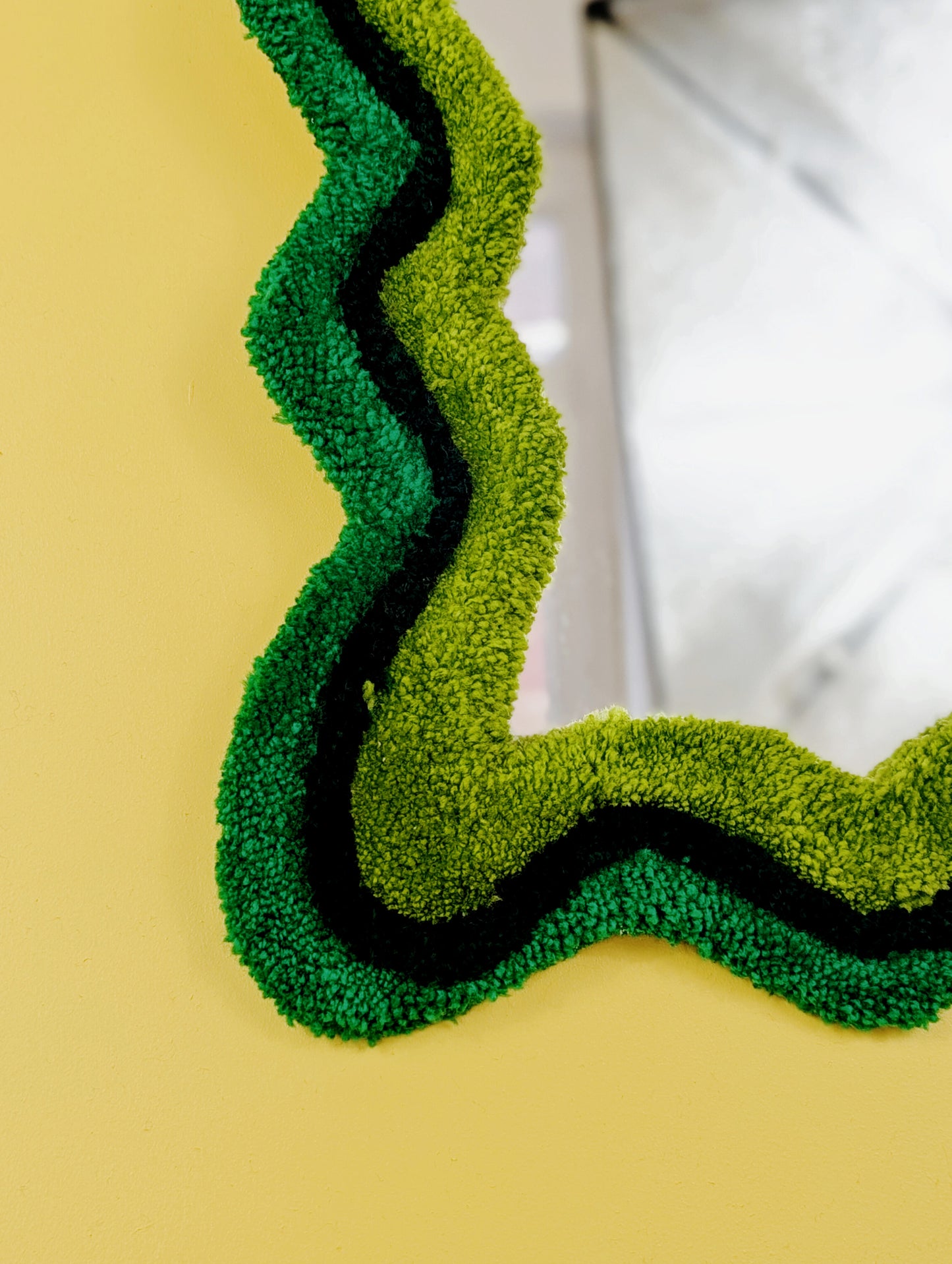 Handmade wavy tufted mirror with colourful textured frame in alternating shades of green, modern aesthetic wall décor for home interiors.