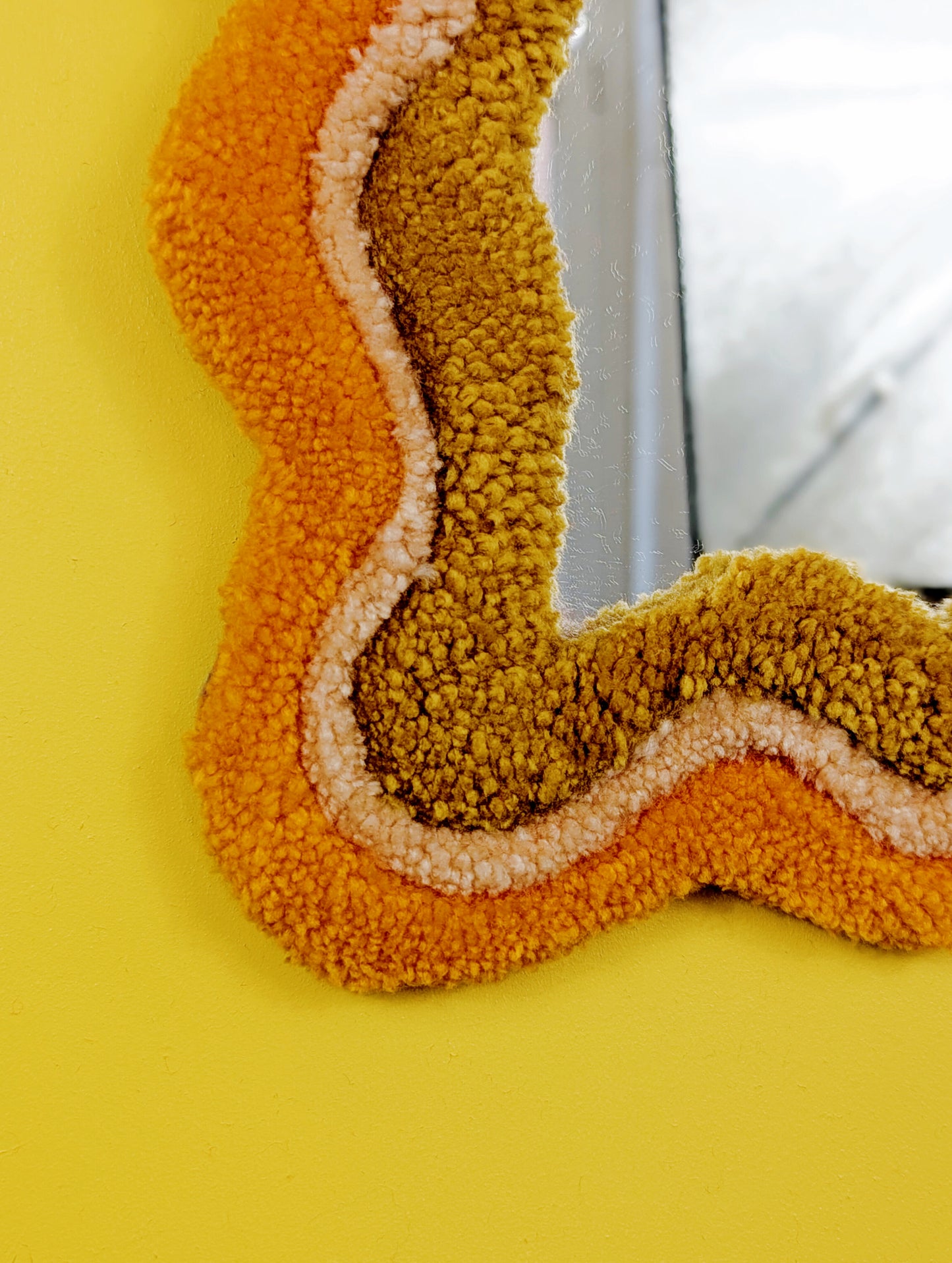 Handmade wavy tufted mirror with colourful textured frame in alternating shades of orange, cream and mustard yellow, modern aesthetic wall décor for home interiors.