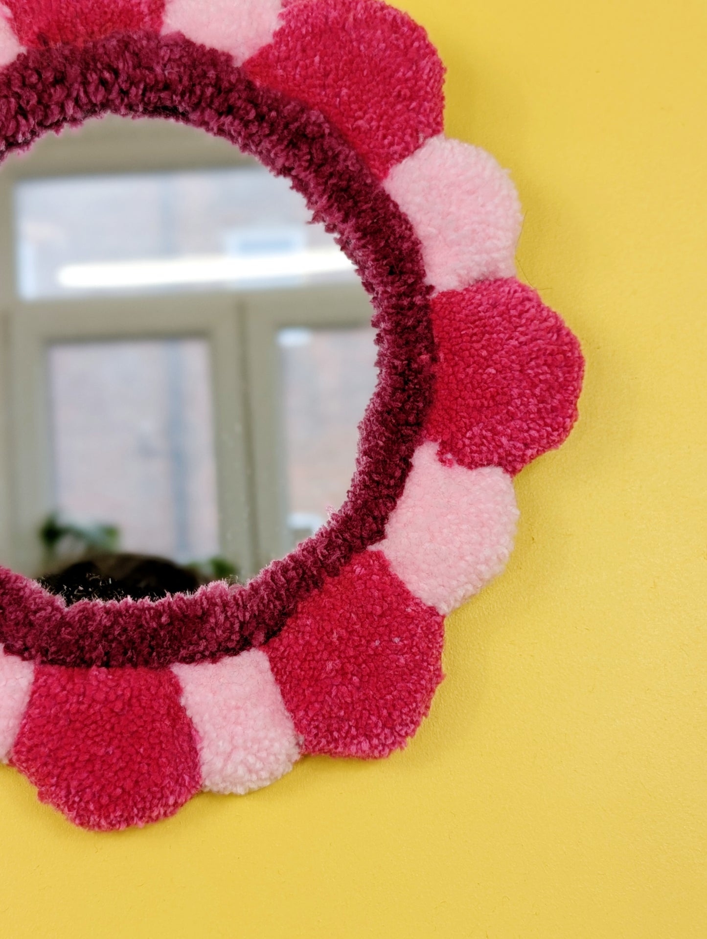 Handmade tufted petal mirror with pink textured yarn petals surrounding a round mirror