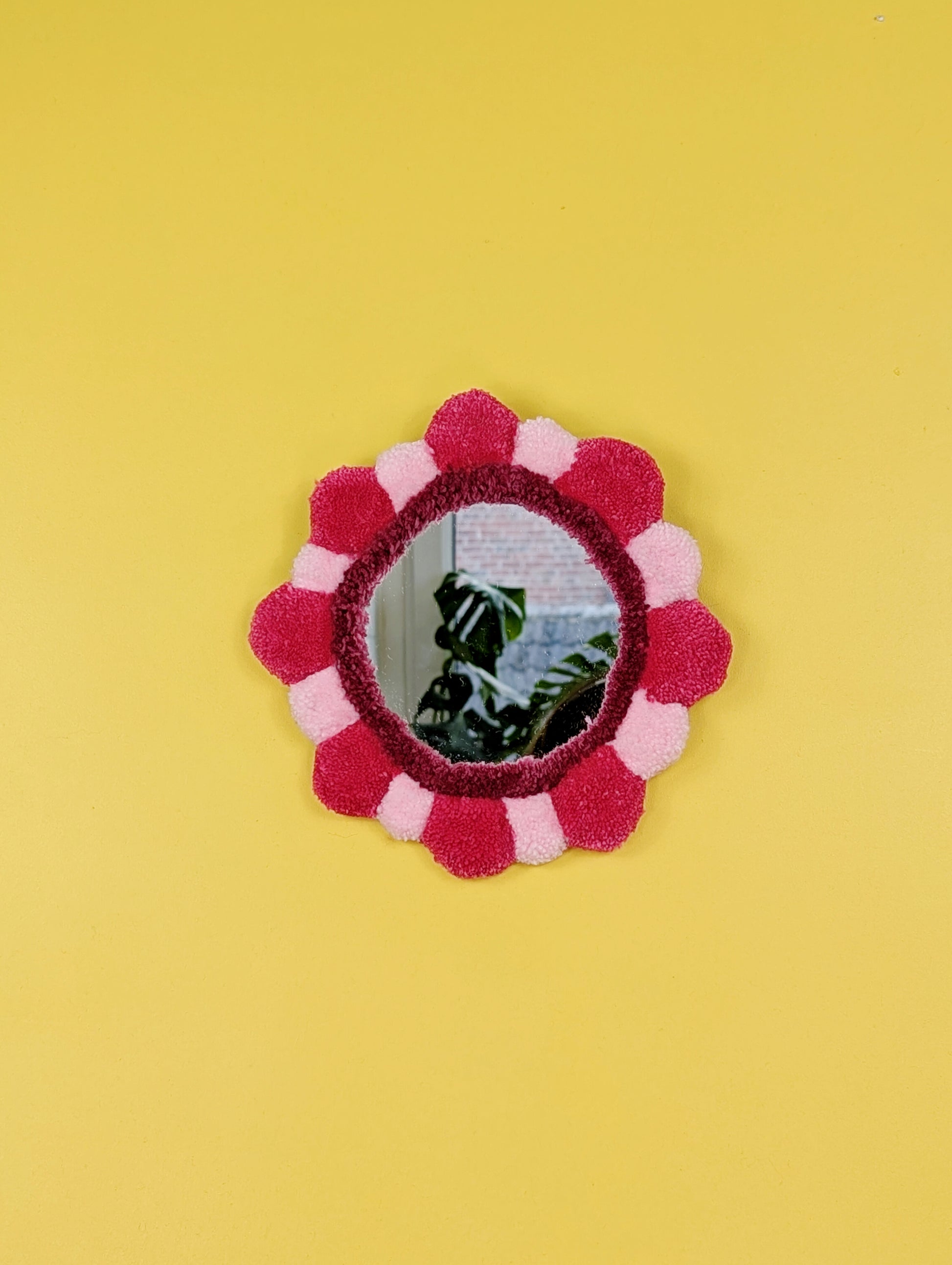 Handmade tufted petal mirror with pink textured yarn petals surrounding a round mirror