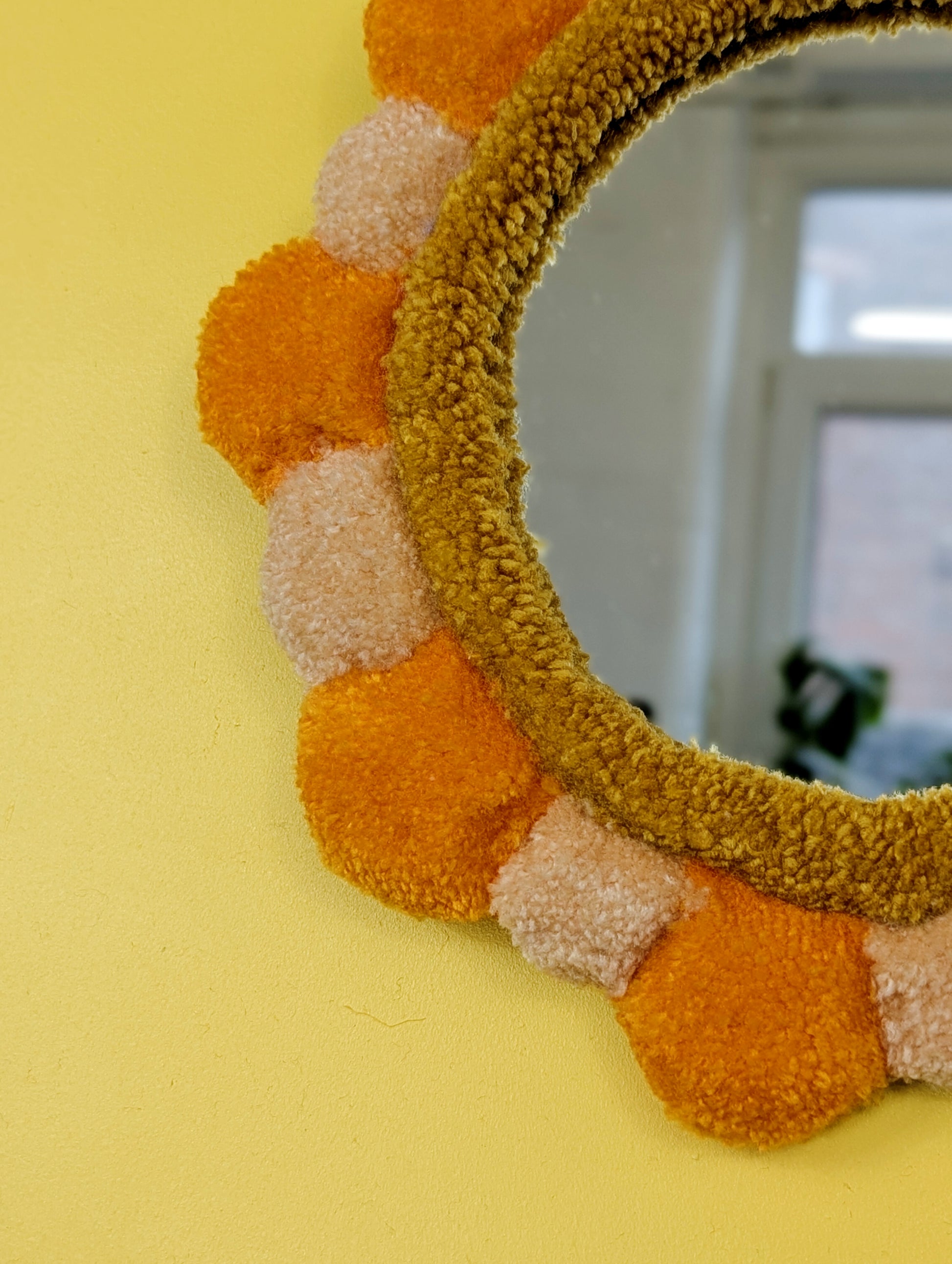 Handmade tufted petal mirror with alternating orange and beige textured yarn petals surrounding a round mirror