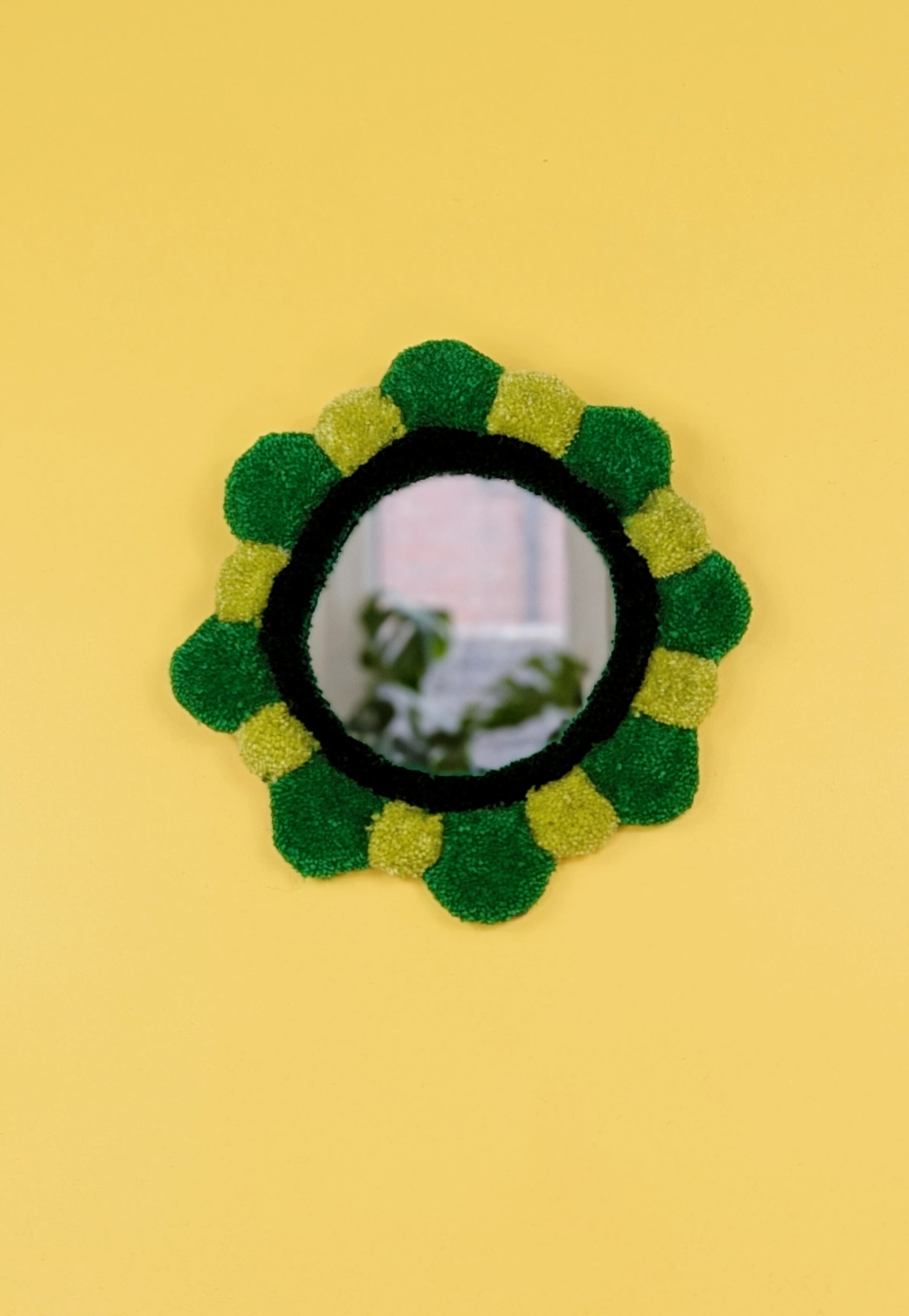 Handmade tufted petal mirror with green textured yarn petals surrounding a round mirror
