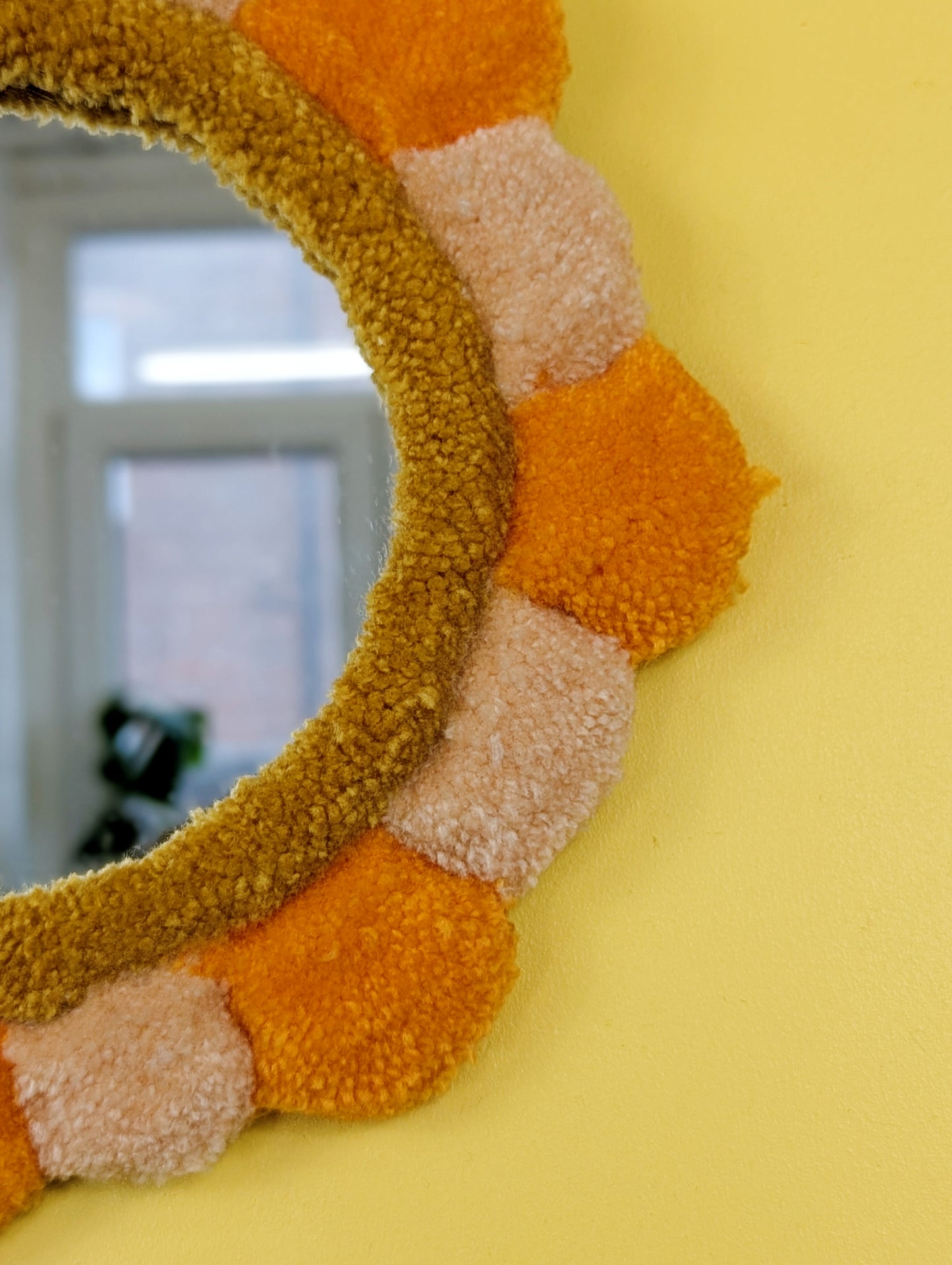 Handmade tufted petal mirror with alternating orange and beige textured yarn petals surrounding a round mirror