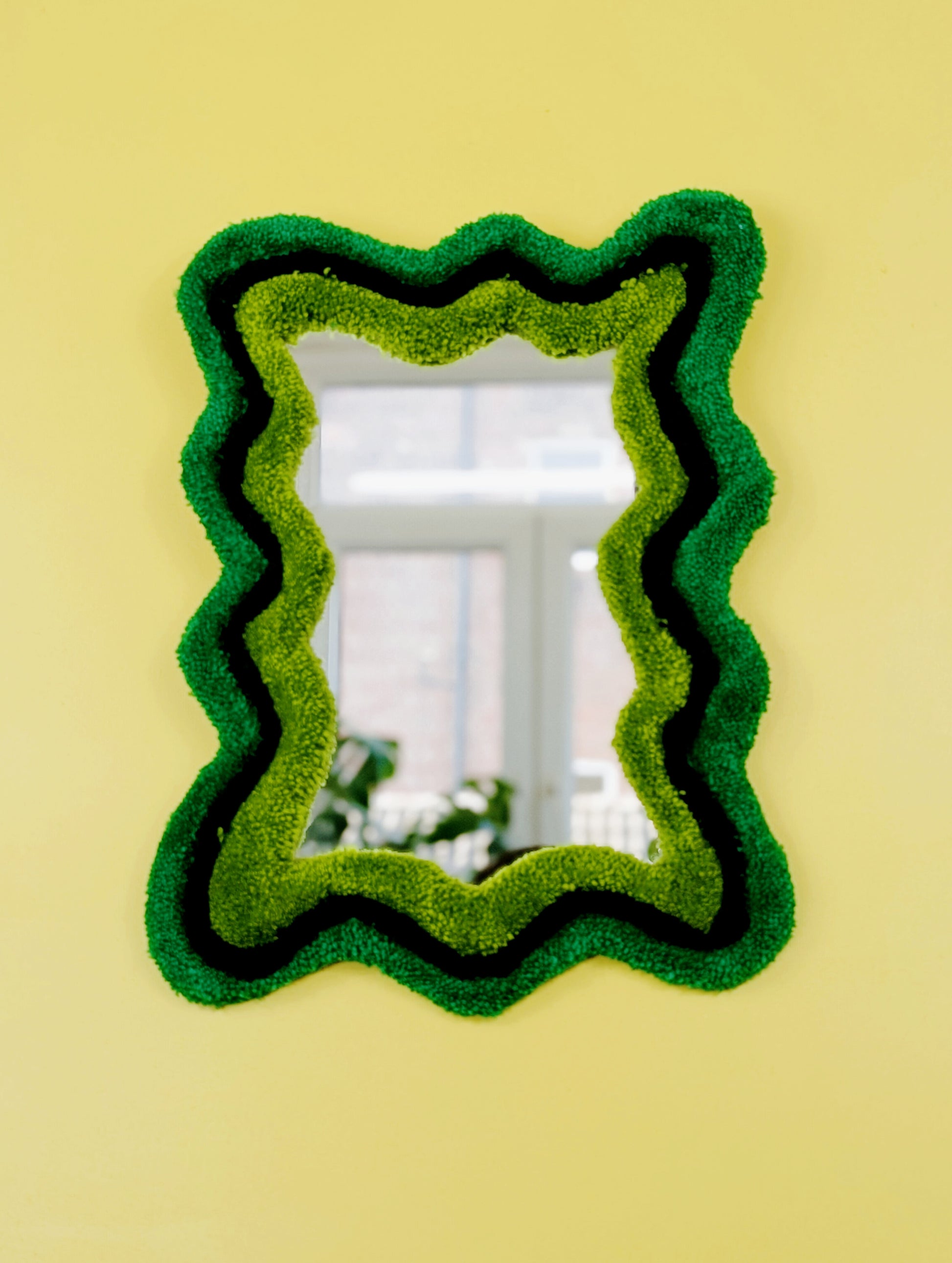 Handmade wavy tufted mirror with colourful textured frame in alternating shades of green, modern aesthetic wall décor for home interiors.