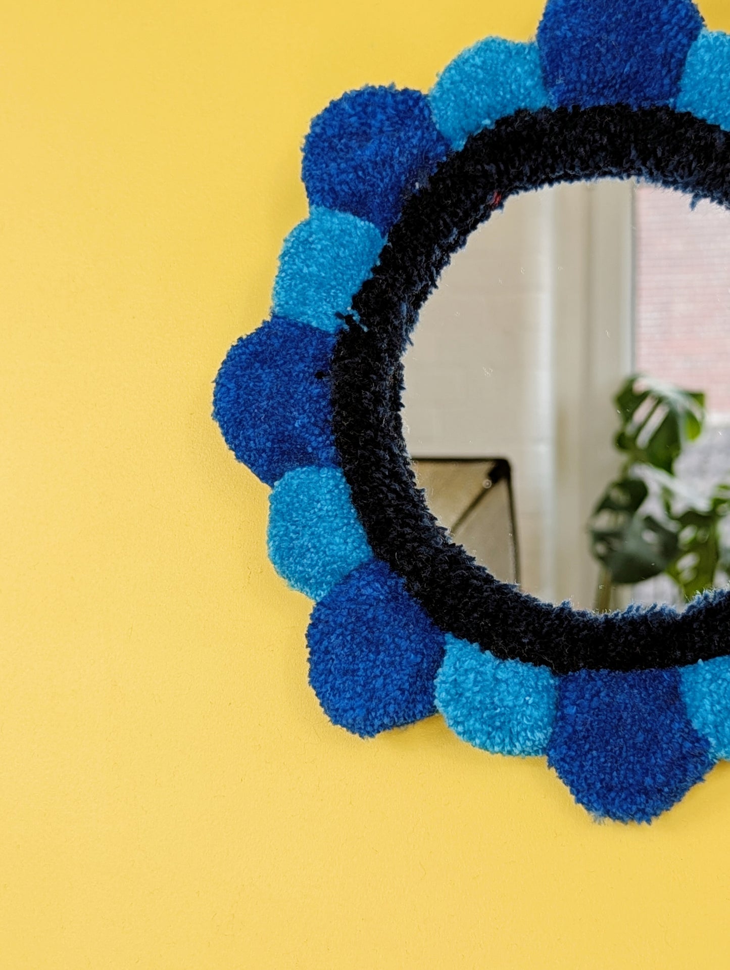 Handmade tufted petal mirror with blue textured yarn petals surrounding a round mirror