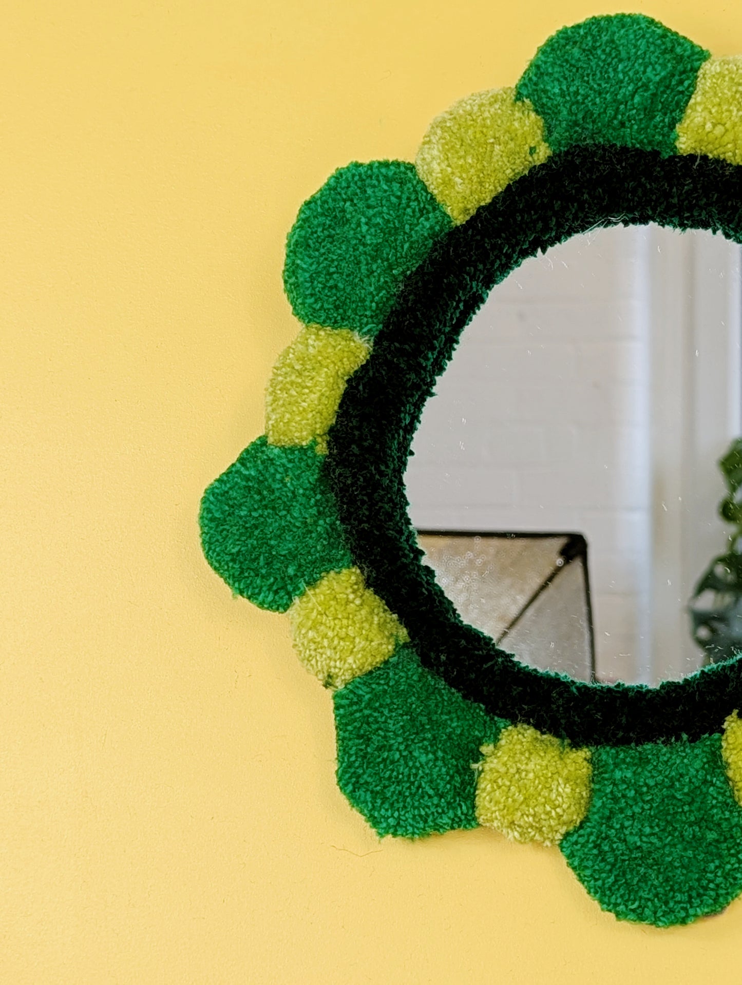 Handmade tufted petal mirror with green textured yarn petals surrounding a round mirror