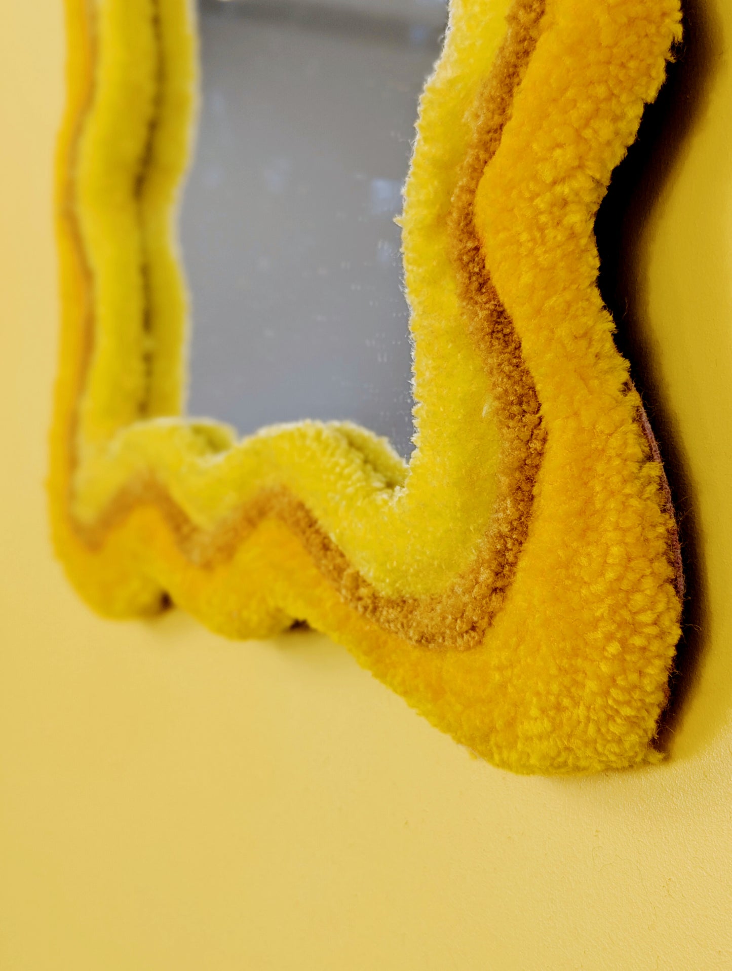 Handmade wavy tufted mirror with colourful textured frame in alternating shades of sunshine yellow, mustard yellow and bright yellow, modern aesthetic wall décor for home interiors.