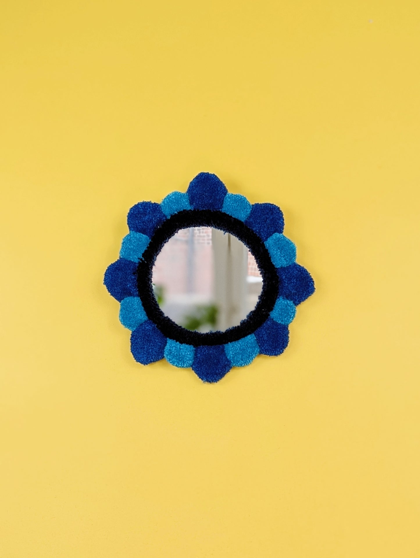 Handmade tufted petal mirror with blue textured yarn petals surrounding a round mirror