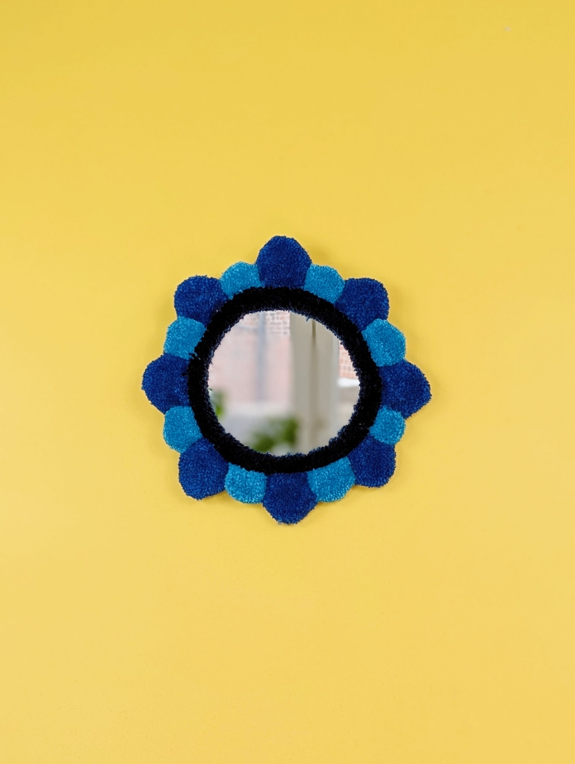Handmade tufted petal mirror with blue textured yarn petals surrounding a round mirror