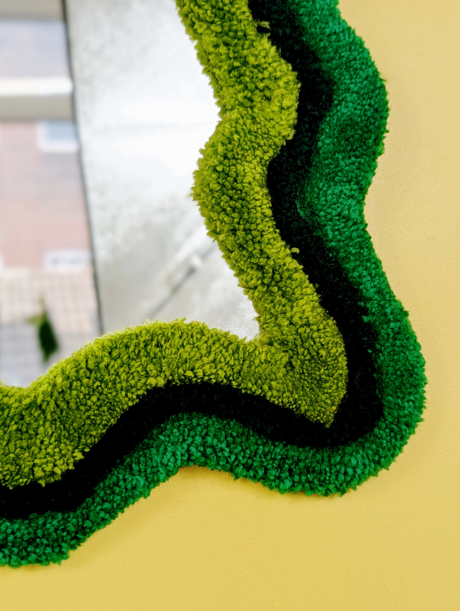Handmade wavy tufted mirror with colourful textured frame in alternating shades of green, modern aesthetic wall décor for home interiors.