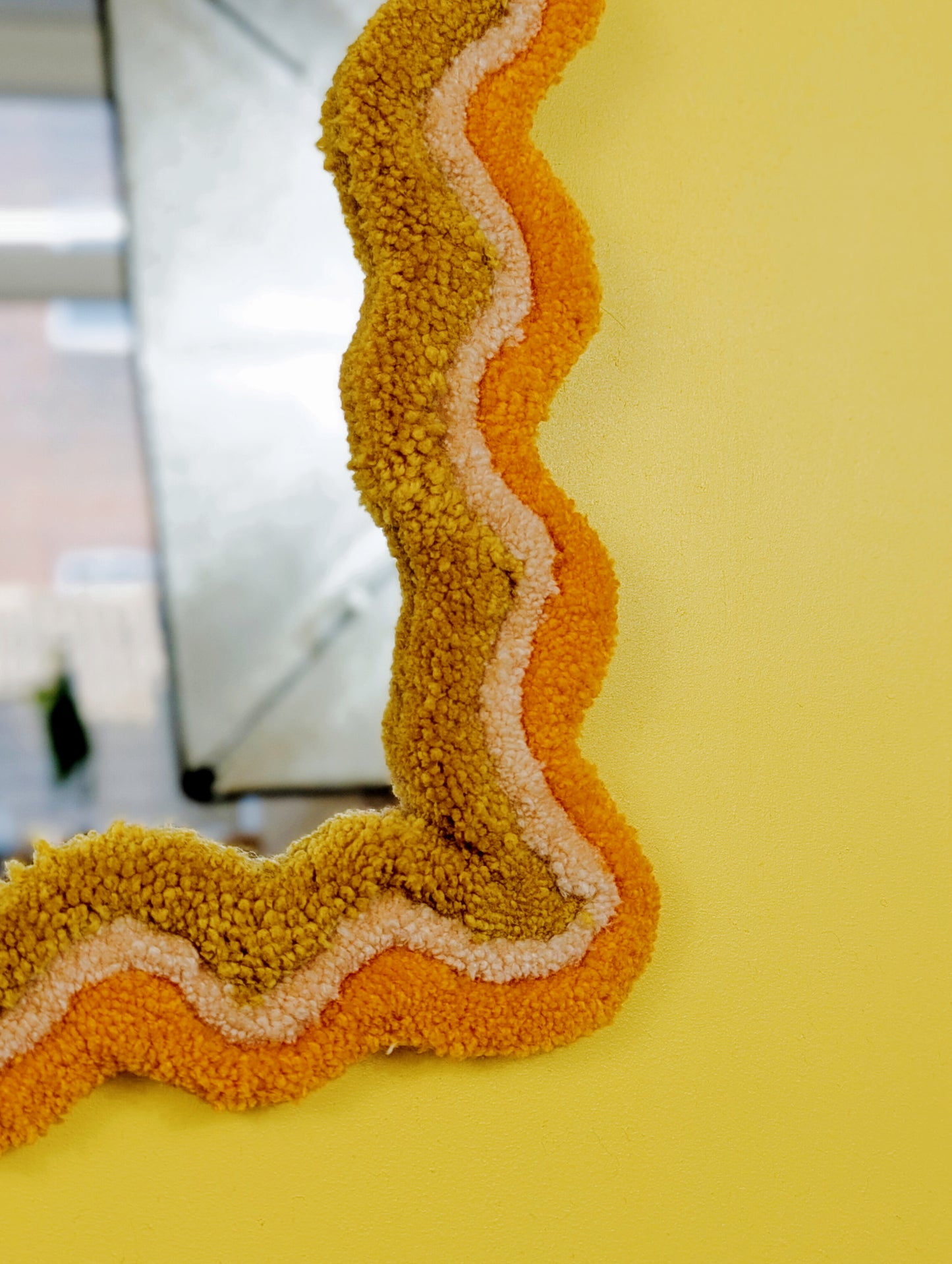 Handmade wavy tufted mirror with colourful textured frame in alternating shades of orange, cream and mustard yellow, modern aesthetic wall décor for home interiors.