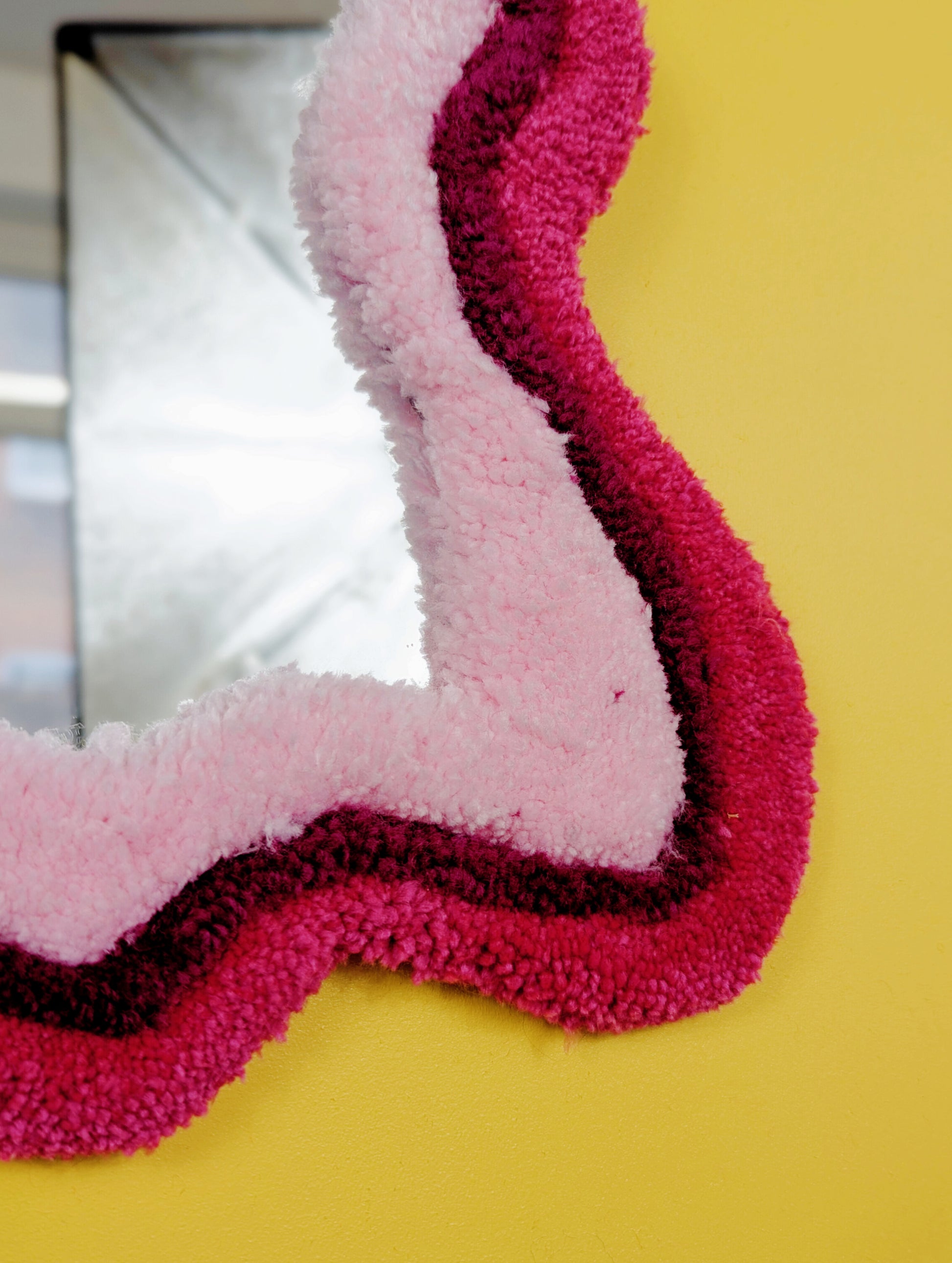 Handmade wavy tufted mirror with colourful textured frame in alternating shades of pink, modern aesthetic wall décor for home interiors.