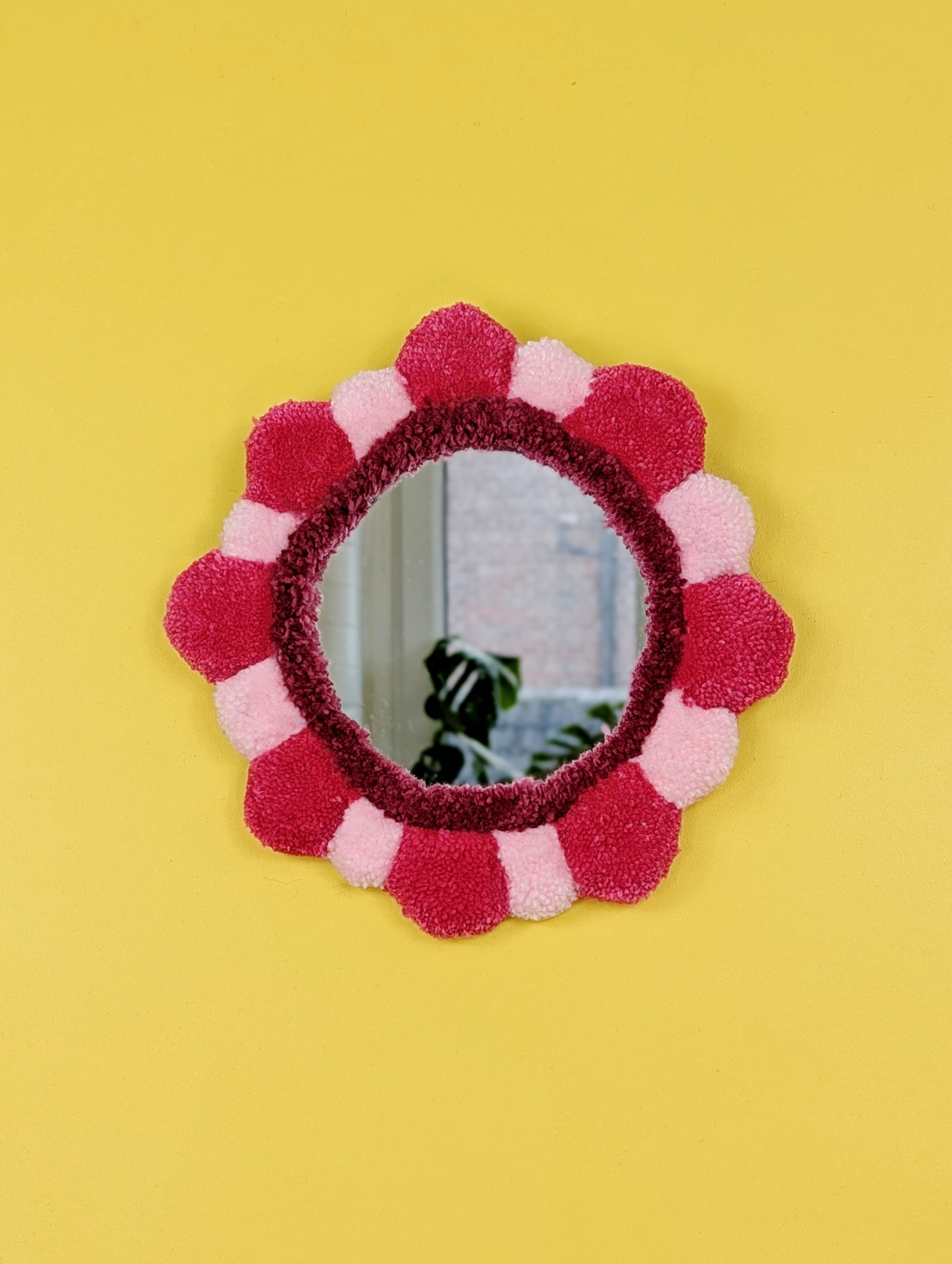 Handmade tufted petal mirror with pink textured yarn petals surrounding a round mirror
