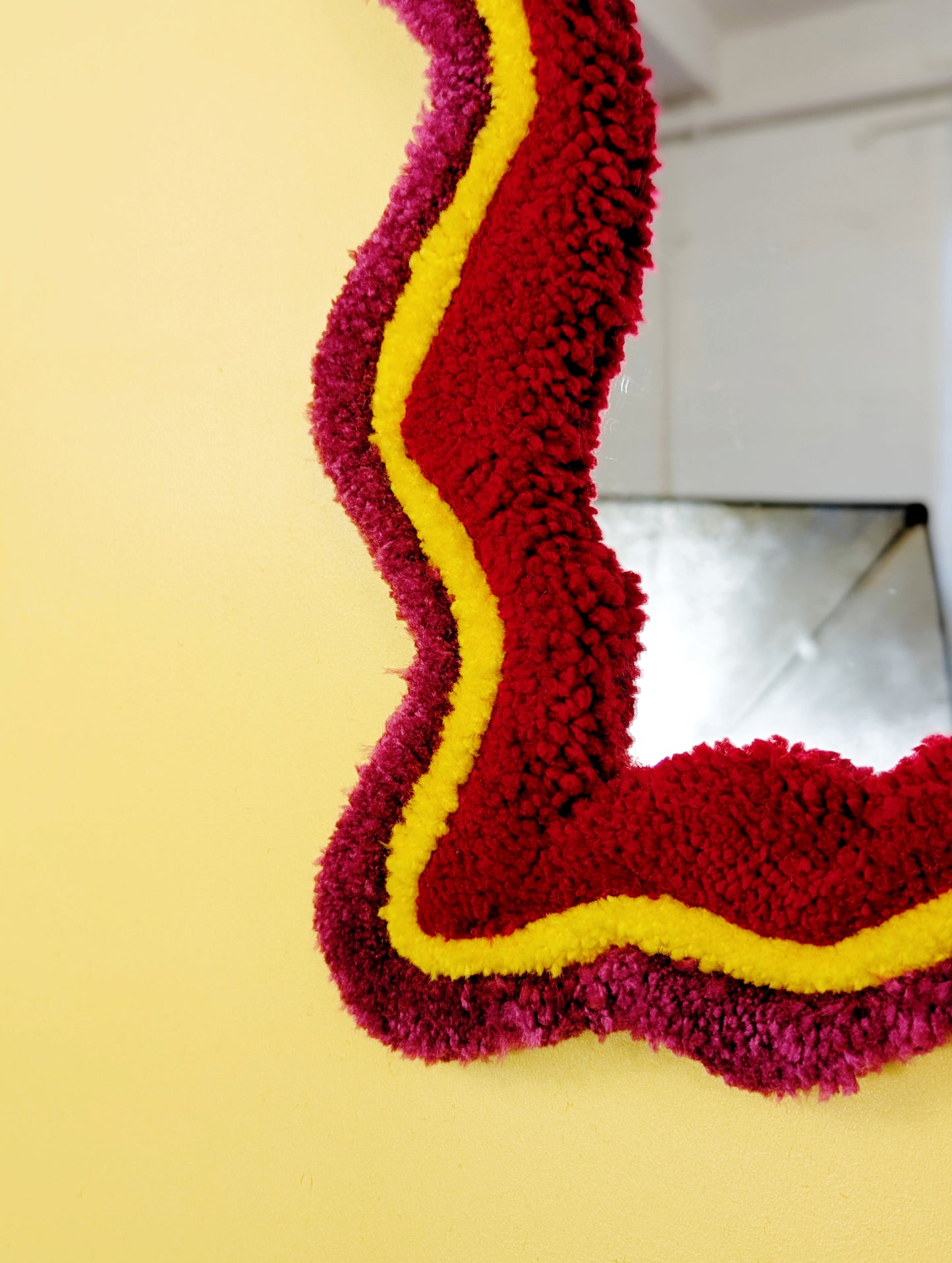 Handmade wavy tufted mirror with colourful textured frame in dark pink, bright yellow and red, modern aesthetic wall décor for home interiors.